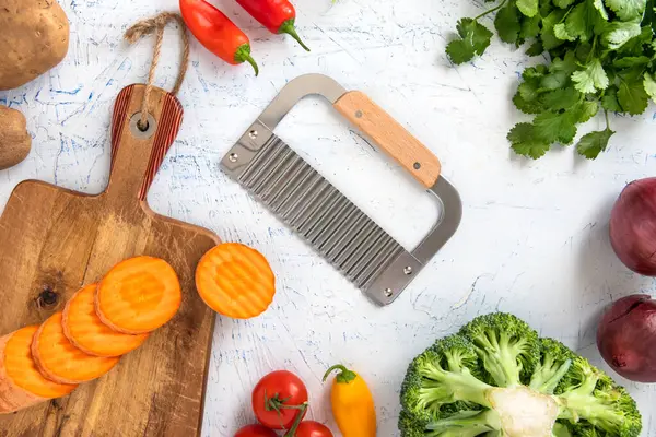 wavy knife for curly slicing vegetables. Carrot slices on a cutting board. Onions, broccoli, tomatoes and parsley top view.