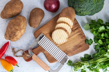 Kıvırcık sebzeler için dalgalı bıçak. Kesme tahtasındaki patates dilimleri. Soğan, brokoli ve maydanoz..