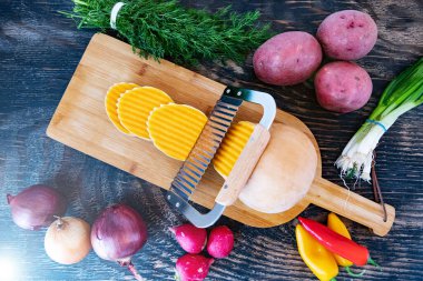 Kesme tahtasında dalga bıçağıyla kesilmiş bir balkabağı. Tahta bir masada çeşitli sebzeler. Yukarıdan görüntüle.