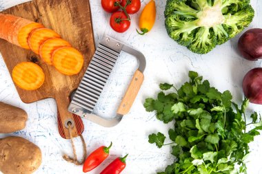 Kıvırcık sebzeler için dalgalı bıçak. Kesme tahtasındaki havuç dilimleri. Soğan, brokoli, domates ve maydanoz..