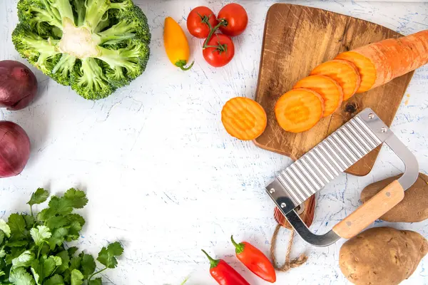 Kıvırcık sebzeler için dalgalı bıçak. Kesme tahtasındaki havuç dilimleri. Soğan, brokoli, domates ve maydanoz manzaralı. Metin için boşluk.