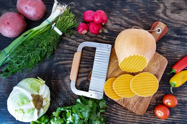 Kesme tahtasında dalga bıçağıyla kesilmiş bir balkabağı. Tahta bir masada çeşitli sebzeler. Yukarıdan görüntüle.