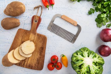 Kıvırcık sebzeler için dalgalı bıçak. Kesme tahtasındaki patates dilimleri. Soğan, brokoli ve maydanoz..