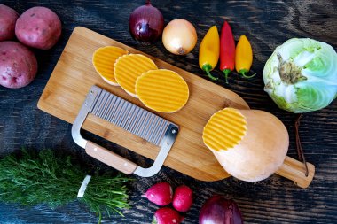 Kesme tahtasında dalga bıçağıyla kesilmiş bir balkabağı. Tahta bir masada çeşitli sebzeler. Yukarıdan görüntüle.