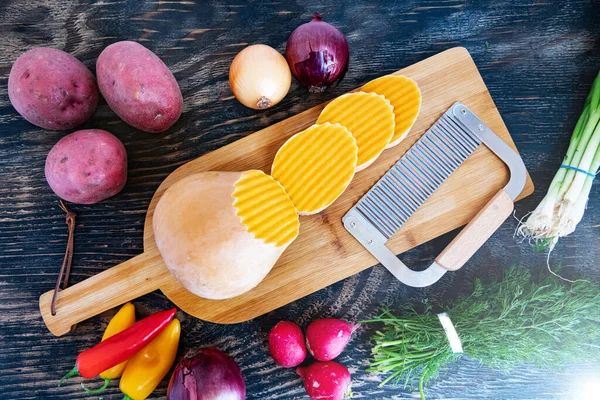 Kesme tahtasında dalga bıçağıyla kesilmiş bir balkabağı. Tahta bir masada çeşitli sebzeler. Yukarıdan görüntüle.