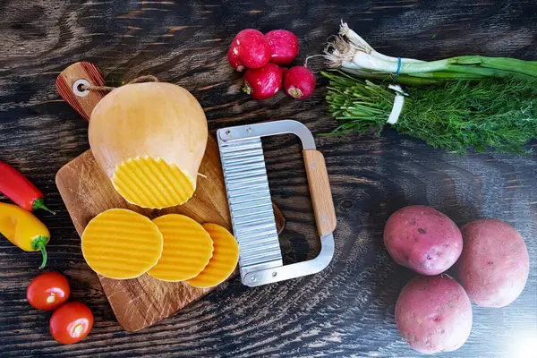 Kesme tahtasında dalga bıçağıyla kesilmiş bir balkabağı. Tahta bir masada çeşitli sebzeler. Yukarıdan görüntüle.