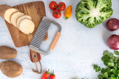 Kıvırcık sebzeler için dalgalı bıçak. Kesme tahtasındaki patates dilimleri. Soğan, brokoli ve maydanoz..
