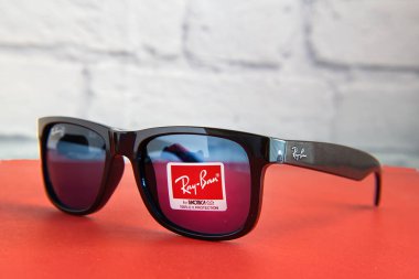 Siyah Ray-Ban güneş gözlüğü ve kırmızı bir masanın üzerinde plastik çerçeveli logo..