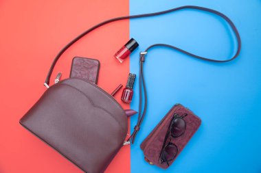 Kırmızı renkli kadın çantası ve kırmızı-mavi arka planda aksesuarlar. Üst görünüm.