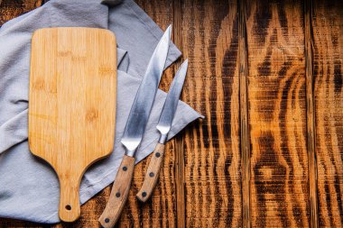 Tahta kesme tahtası, peçete ve tahta bir masada bir çift bıçak. Metin için boşluk.