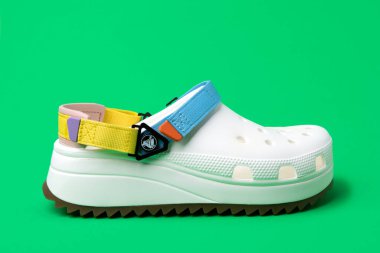 Yeşil arka planda renkli kayışları olan beyaz timsahlar. Lastik sandaletler, moda plaj ayakkabıları..