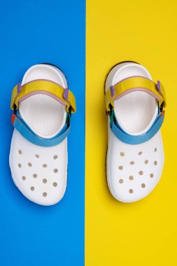 Sarı ve mavi arka planı olan beyaz timsah terlikleri. Rahat unisex plaj ayakkabıları.