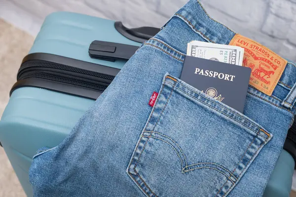 レヴィのジーンズ アメリカのパスポートとドルがスーツケースに横たわっている トラベルコンセプト ロイヤリティフリーのストック画像