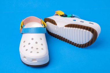 Mavi arka planda renkli kayışlı beyaz timsah sandaletleri..