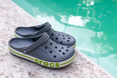 Gri Crocs sandaletleri havuzun kenarında yatıyor. Moda konforlu plaj ayakkabıları.