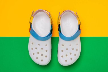 Sarı-yeşil arka planda belirgin bir tasarımı olan beyaz Crocs sandaletleri.