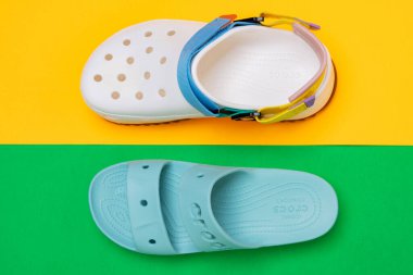 Sarı-yeşil arka planda belirgin bir tasarımı olan beyaz Crocs sandaletleri.