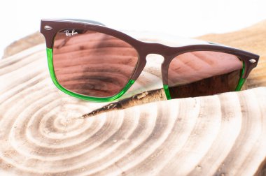 Tahta bir kütüğün üzerinde yeşil çerçeveli Ray-Ban güneş gözlüğü.