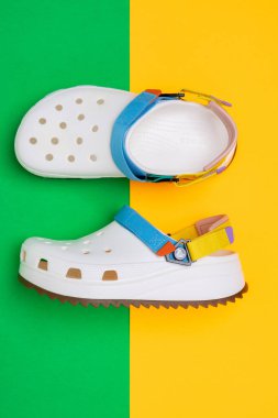 Sarı-yeşil arka planda belirgin bir tasarımı olan beyaz Crocs sandaletleri.