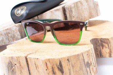 Tahta bir kütüğün üzerinde yeşil çerçeveli Ray-Ban güneş gözlüğü.
