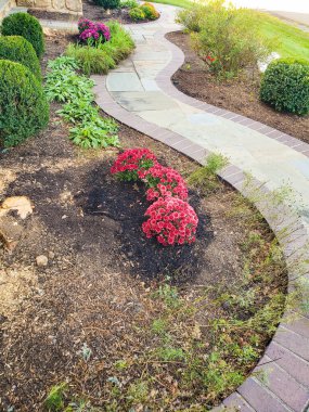 Çalılar ve çiçekler arasında dolambaçlı taş patika ve peyzaj.