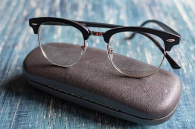 Klasik optik gözlükler ve mavi bir masanın üzerindeki çanta..