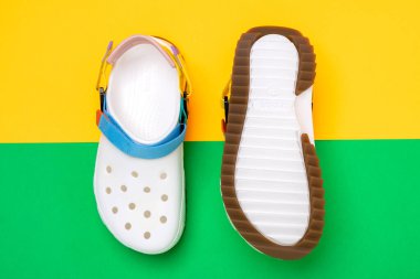 Sarı-yeşil arka planda belirgin bir tasarımı olan beyaz Crocs sandaletleri.