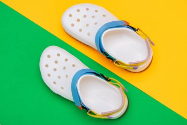 Sarı-yeşil arka planda belirgin bir tasarımı olan beyaz Crocs sandaletleri.