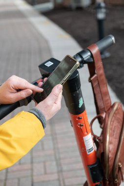Kadın şehirde elektrikli scooter kiralamak için mobil uygulamasını kullanıyor..