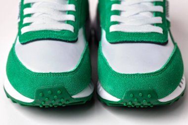 Beyaz arka planda beyaz ve yeşil spor ayakkabıları yakın plan.