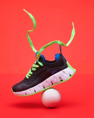 Black sports sneakers reebok with bright green sole and ball on red background. clipart