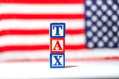 It's tax season. TAX is written in wooden letters on a background of a blurred American flag. clipart