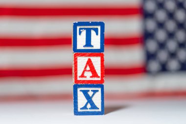 TAX lettering made of wooden cubes on an American flag background. clipart