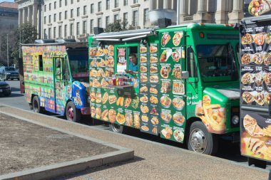 Kaldırımda sokak yemeği var. Minibüsün yanında parlak renkli etiketli sokak yemeği minibüsü..