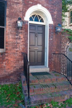 Çekici tuğlalı eski bir ev, merdivenleri ve parmaklıkları olan ahşap bir kapı..