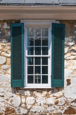 Duvarında panjurlar olan bir pencere, ön cephesinde pencere olan eski bir taş evin duvarı.