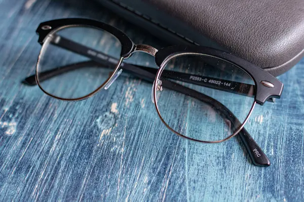 Mavi bir masada, diyopterli ve gri gözlüklü optik gözlük.