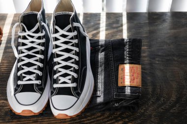 Converse spor ayakkabıları ve Levi 'nin kotu ahşap bir masada. Perdelerden ışık geliyor..