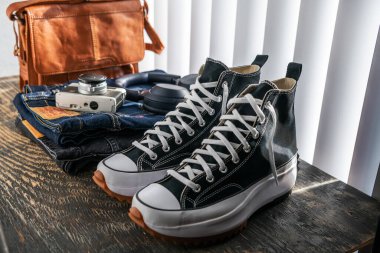 Converse spor ayakkabıları, Levi 'nin kotu, kulaklıklar ve tahta bir masada bir çanta..