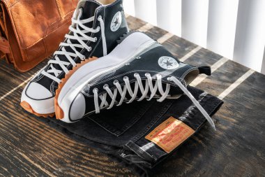 Converse spor ayakkabıları, Levi 'ın kotu ve tahta masada bir çanta. Perdelerden ışık geliyor..