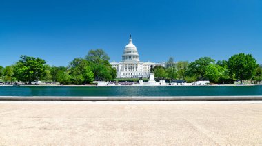 Washington 'daki ABD Kongre Binası' nın panoramik manzarası. Capitol mavi bulutların altında yeşil ağaçlarla çevrili..