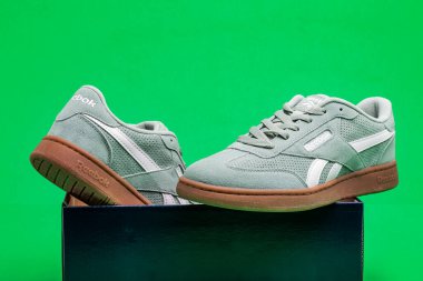 Yeşil arka planda yumuşak süet Reebok spor ayakkabıları ve damgalı kutu..