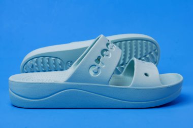 Açık mavi arka planda bir çift kadın mavi Crocs sandaleti.