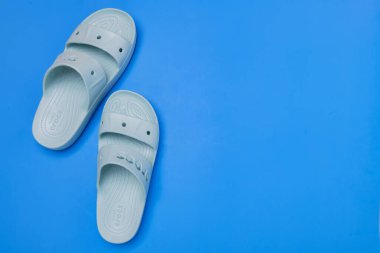 Açık mavi arka planda bir çift kadın mavi Crocs sandaleti. Metin için boşluk.