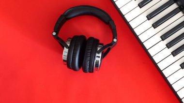 Kulaklıklar ve elektronik piyano anahtarları kırmızı arka planda, üst manzara. Yaratıcılık kavramı. Metin için yer.
