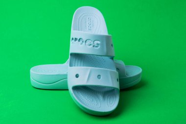 Yeşil arka planda imzası olan bir çift mavi Crocs sandaleti..