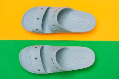 Sarı ve yeşil arka planda bir çift kadın mavi Crocs sandaleti. Üst görünüm.