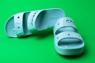 Yeşil arka planda imzası olan bir çift mavi Crocs sandaleti..
