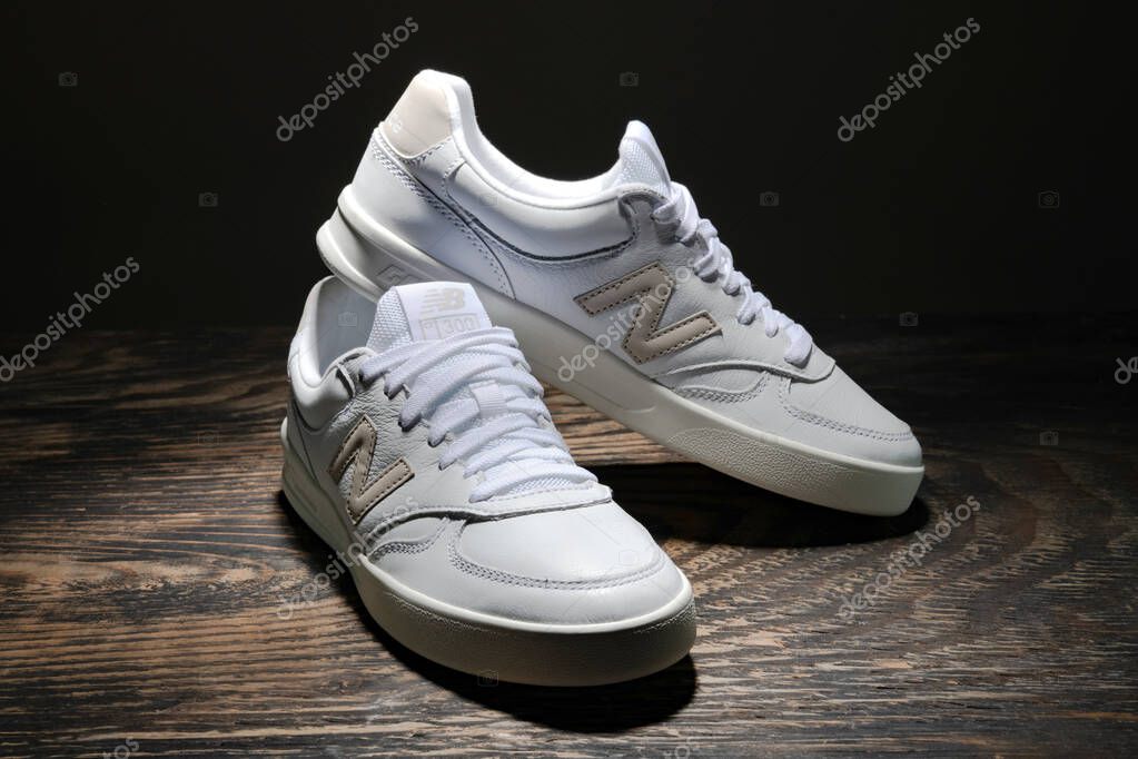White leather New Balance sneakers on a dark wooden background.