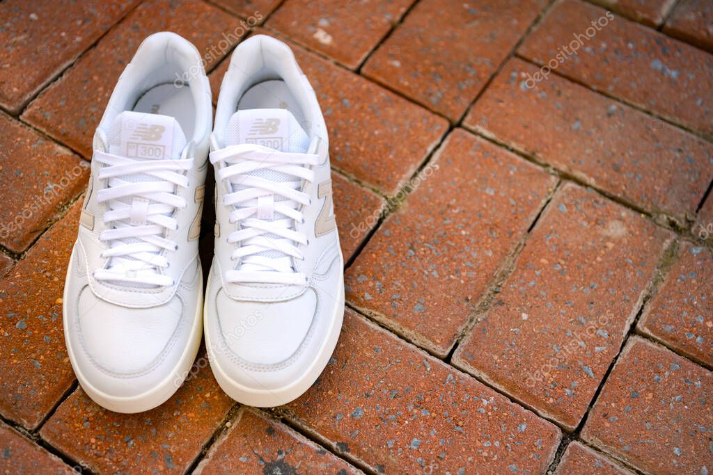 White leather New Balance sneakers on a brick sidewalk. Athletic casual shoes.